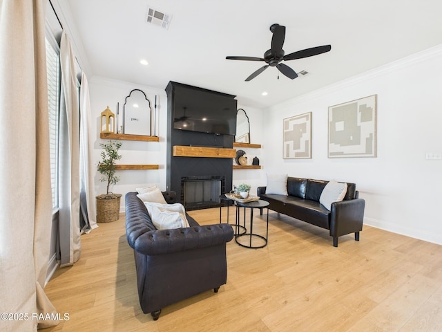 living area featuring visible vents, wood finished floors, a fireplace, and ornamental molding