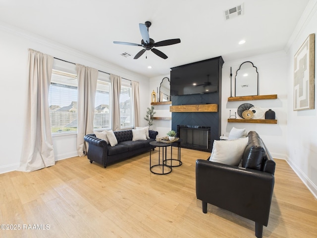 living room featuring light wood-type flooring, visible vents, a ceiling fan, a fireplace, and baseboards