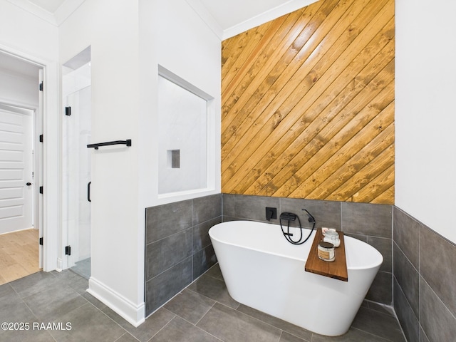 bathroom featuring tile walls, wood walls, crown molding, tile patterned flooring, and a freestanding bath