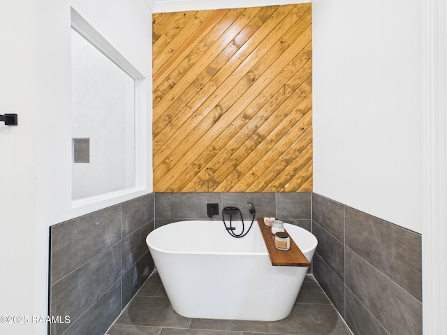 full bath featuring a freestanding tub, tile walls, wood walls, and tile patterned flooring