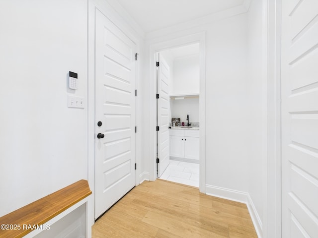 hall featuring a sink, baseboards, and light wood-style flooring