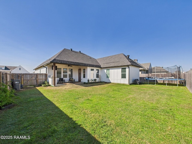 back of property featuring a trampoline, a fenced backyard, a lawn, and ceiling fan