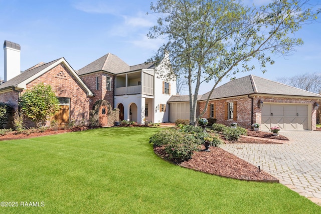 view of front of property featuring an attached garage, a balcony, brick siding, decorative driveway, and a front lawn