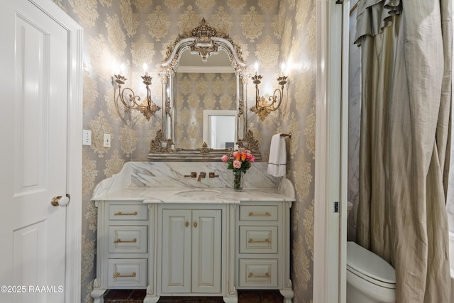 bathroom with vanity, toilet, and wallpapered walls