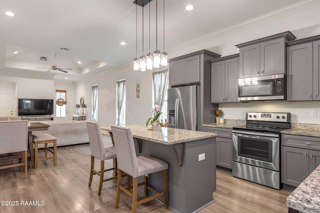 kitchen with light stone counters, open floor plan, gray cabinets, stainless steel appliances, and pendant lighting