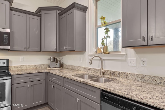 kitchen featuring stainless steel appliances, a sink, light stone counters, and gray cabinetry