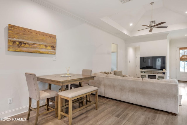 living area featuring wood finished floors, visible vents, baseboards, vaulted ceiling, and ornamental molding