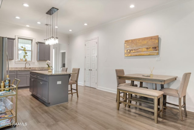 kitchen with a center island, pendant lighting, gray cabinetry, light wood-style floors, and light stone countertops