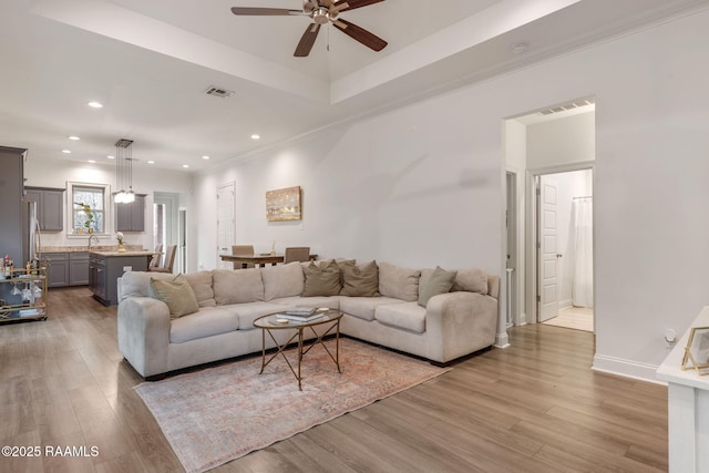 living area with light wood finished floors, visible vents, a raised ceiling, ornamental molding, and recessed lighting