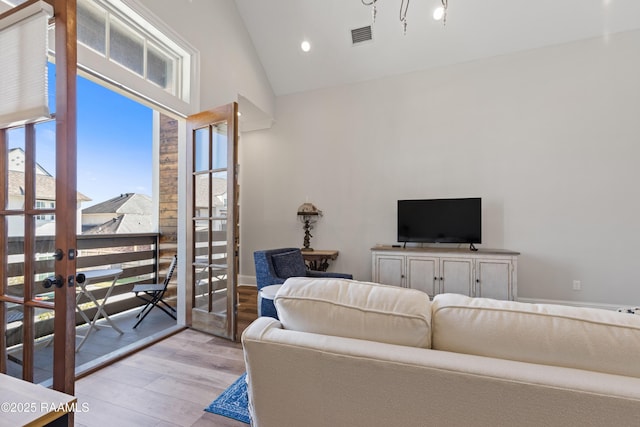 living room with visible vents, high vaulted ceiling, plenty of natural light, and light wood-style flooring