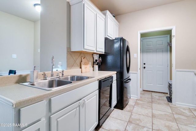 kitchen with light tile patterned floors, wainscoting, black appliances, white cabinetry, and a sink