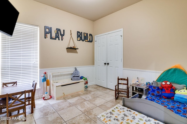 bedroom with light tile patterned floors, a closet, and wainscoting