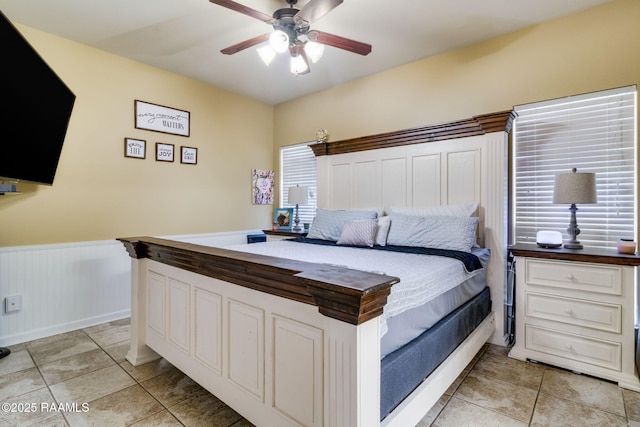 bedroom with a wainscoted wall, ceiling fan, and light tile patterned floors