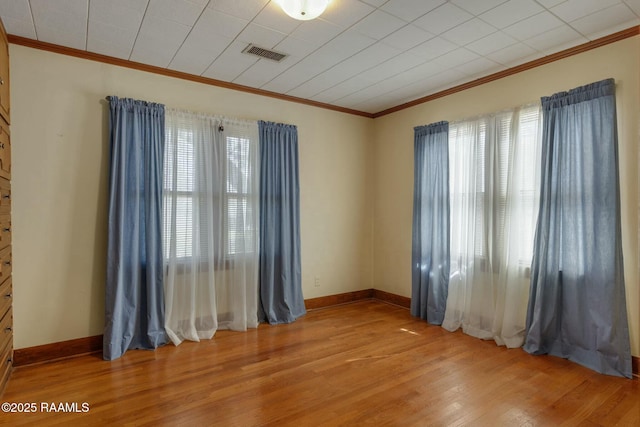 spare room with light wood-type flooring, visible vents, a wealth of natural light, and ornamental molding