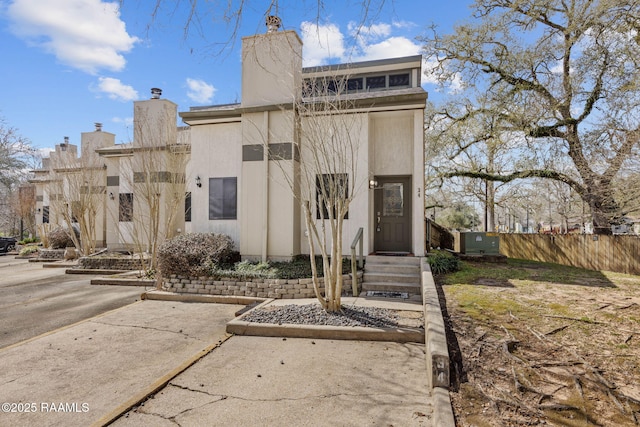 view of front facade with fence, a chimney, and stucco siding