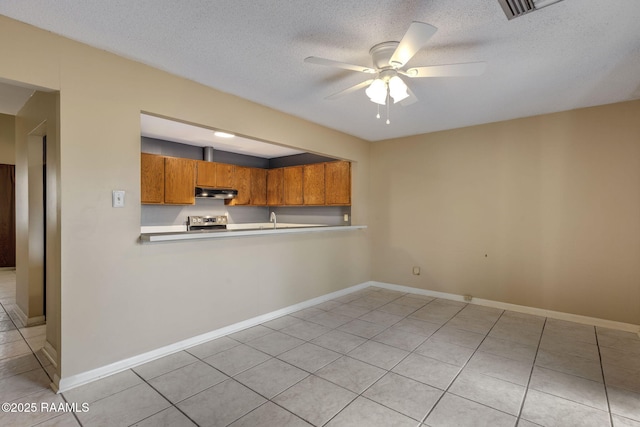 kitchen featuring brown cabinetry, a ceiling fan, light countertops, stainless steel range with electric cooktop, and under cabinet range hood