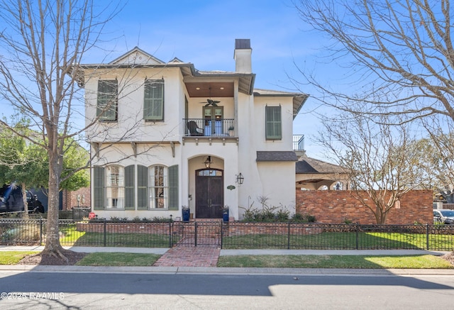 view of front of home with a balcony, a fenced front yard, a chimney, ceiling fan, and stucco siding