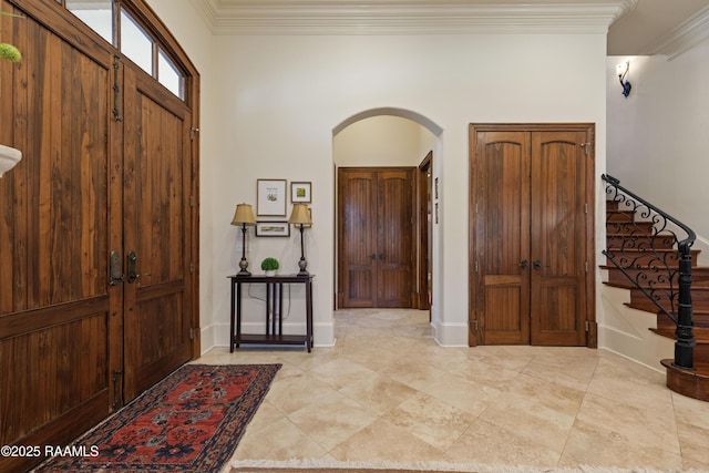 entrance foyer featuring arched walkways, crown molding, stairway, and baseboards