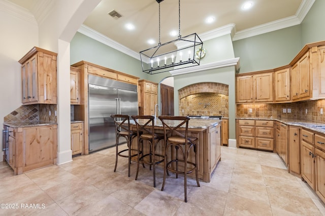 kitchen with arched walkways, built in fridge, a high ceiling, visible vents, and a center island with sink