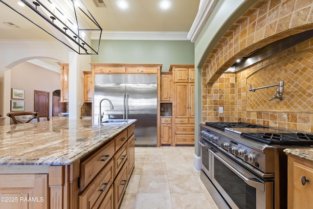 kitchen with premium appliances, arched walkways, ornamental molding, and backsplash