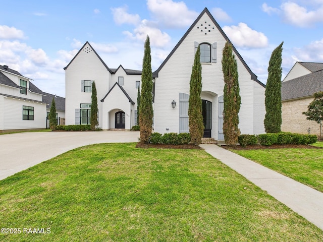 french country home featuring concrete driveway, brick siding, and a front lawn