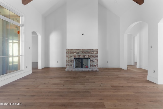 unfurnished living room with high vaulted ceiling, a brick fireplace, and wood-type flooring