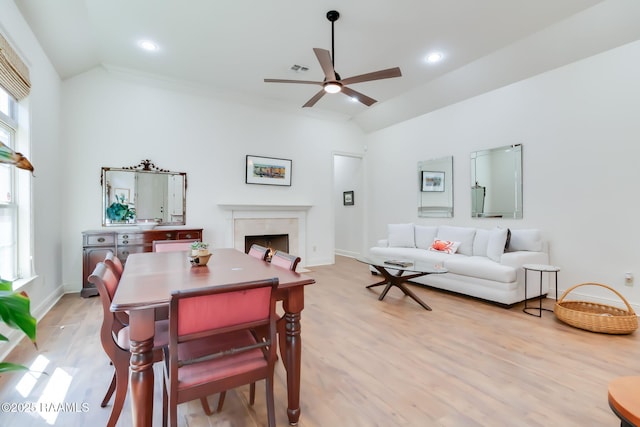 dining area with a high end fireplace, vaulted ceiling, ceiling fan, light wood-type flooring, and baseboards