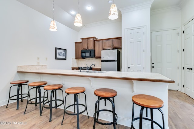 kitchen with pendant lighting, light countertops, freestanding refrigerator, black microwave, and a peninsula