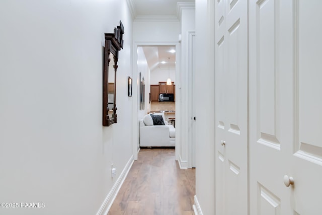 corridor with light wood-style floors, ornamental molding, and baseboards