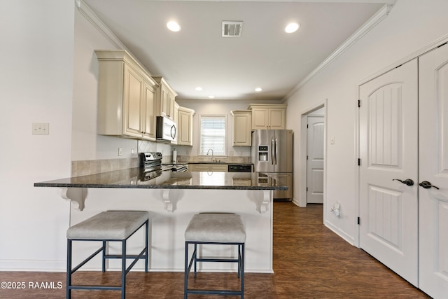 kitchen with cream cabinetry, visible vents, appliances with stainless steel finishes, a peninsula, and a kitchen breakfast bar