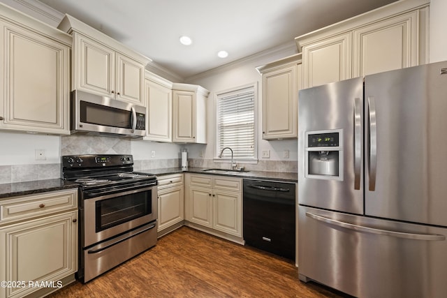 kitchen with appliances with stainless steel finishes, dark wood finished floors, cream cabinetry, and a sink