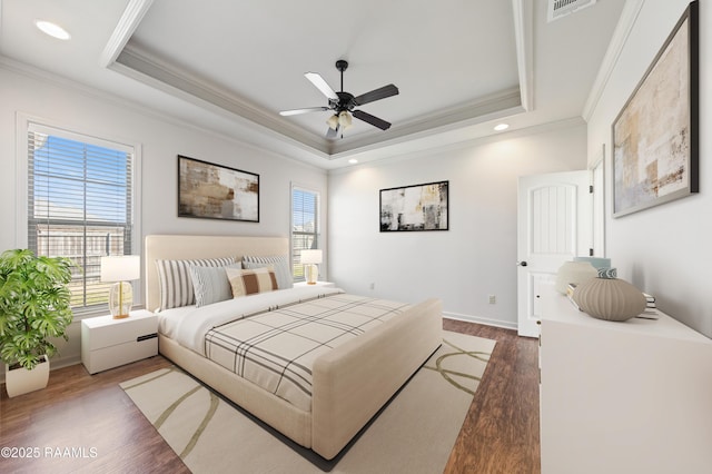 bedroom with a tray ceiling, multiple windows, visible vents, and wood finished floors