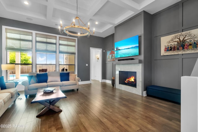 living area with a notable chandelier, coffered ceiling, wood finished floors, a high ceiling, and a lit fireplace