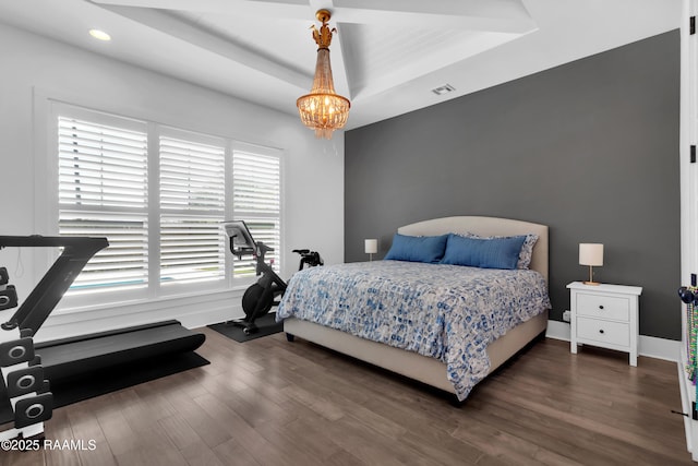 bedroom featuring wood finished floors, a raised ceiling, baseboards, a notable chandelier, and visible vents