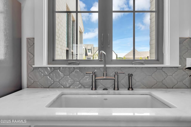 interior details featuring light stone countertops, a sink, and backsplash