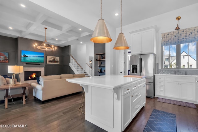 kitchen featuring coffered ceiling, a sink, a lit fireplace, stainless steel refrigerator with ice dispenser, and open floor plan
