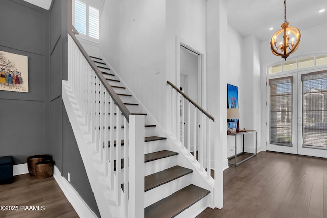 stairway with wood finished floors, baseboards, a high ceiling, a notable chandelier, and recessed lighting
