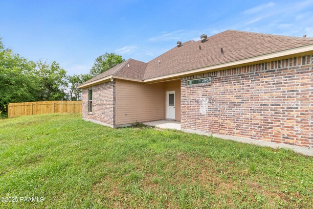 back of house with brick siding, fence, a shingled roof, and a lawn
