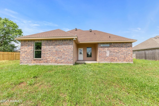rear view of property featuring fence, brick siding, and a yard