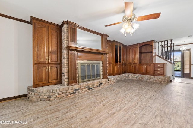 unfurnished living room featuring a brick fireplace, ceiling fan, baseboards, and wood finished floors