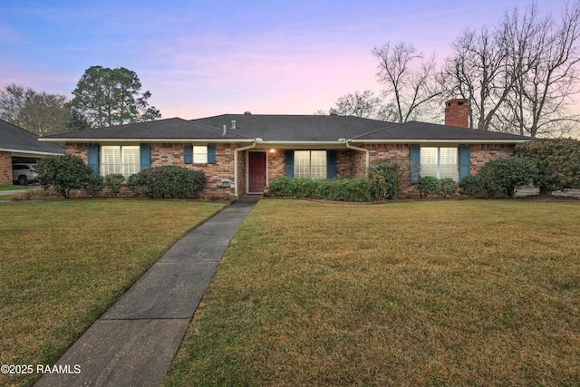 ranch-style home featuring brick siding, a chimney, a front yard, and roof with shingles