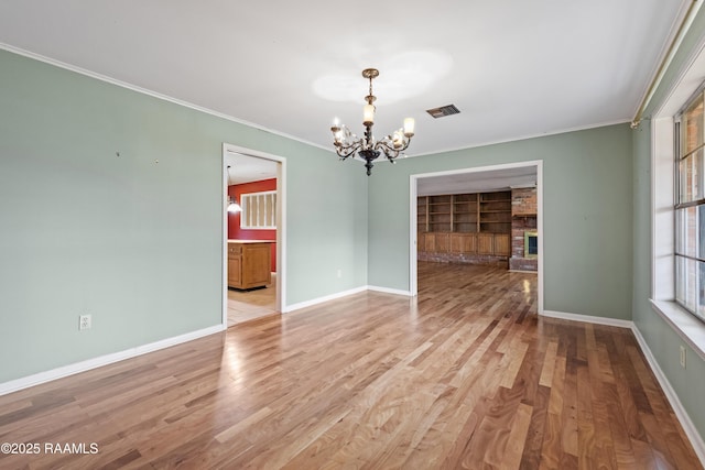 empty room with light wood-style floors, a brick fireplace, a chandelier, and ornamental molding