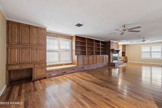 unfurnished living room featuring visible vents, wood-type flooring, a textured ceiling, crown molding, and a brick fireplace