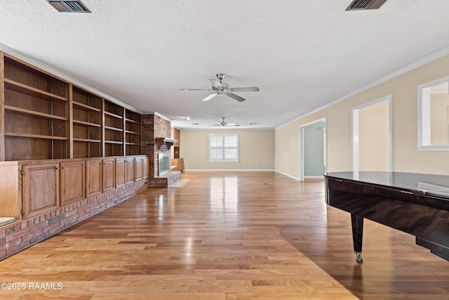 interior space with visible vents, ornamental molding, a textured ceiling, a fireplace, and light wood finished floors
