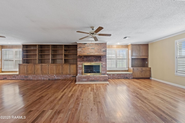 unfurnished living room with light wood-style floors, a brick fireplace, ornamental molding, and a ceiling fan