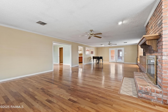 unfurnished living room featuring light wood finished floors, visible vents, a brick fireplace, baseboards, and a textured ceiling