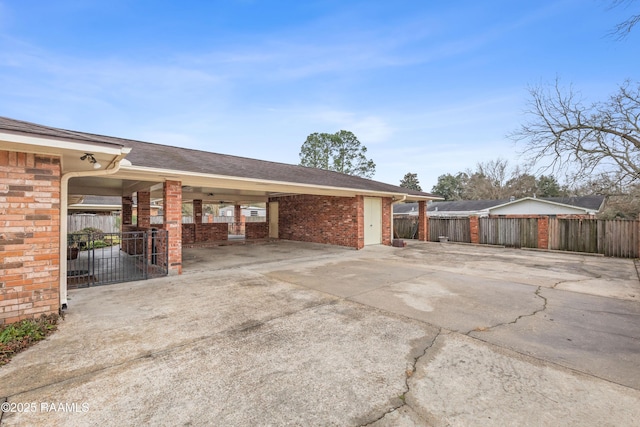 view of home's exterior featuring brick siding, concrete driveway, a carport, and fence