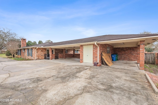view of front of house with an attached carport, fence, a chimney, concrete driveway, and brick siding