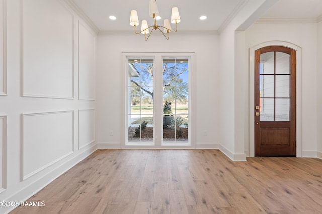 unfurnished dining area featuring baseboards, ornamental molding, light wood-type flooring, and a notable chandelier