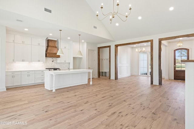 kitchen with a kitchen island with sink, premium range hood, white cabinets, light countertops, and hanging light fixtures